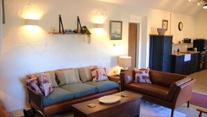 A living room with a sofa, a coffee table, and a chair. There is a kitchen area with cabinets and a sink. - The Hidden Cottage, Ardara, Donegal. (Ardara)