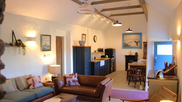 A spacious living area with a sofa, coffee table, and dining table. A kitchen is visible in the background. - The Hidden Cottage, Ardara, Donegal. (Ardara)
