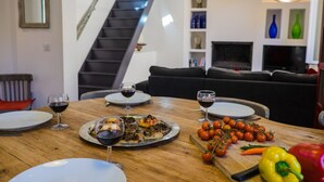 Een eettafel met borden, wijnglazen en eten, een trap, een bank en decoratieve objecten in een woonruimte.