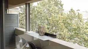 Een modern balkon met een glazen balustrade, een zithoek met een stoel en een tafel, en drie hangende bolvormige lampen.