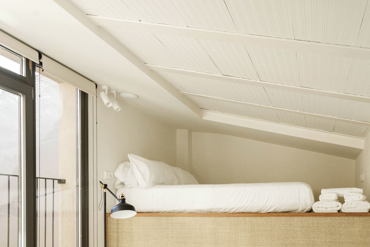 A bedroom with a bunk bed, a small wooden stool, a bedside table, and a lamp.