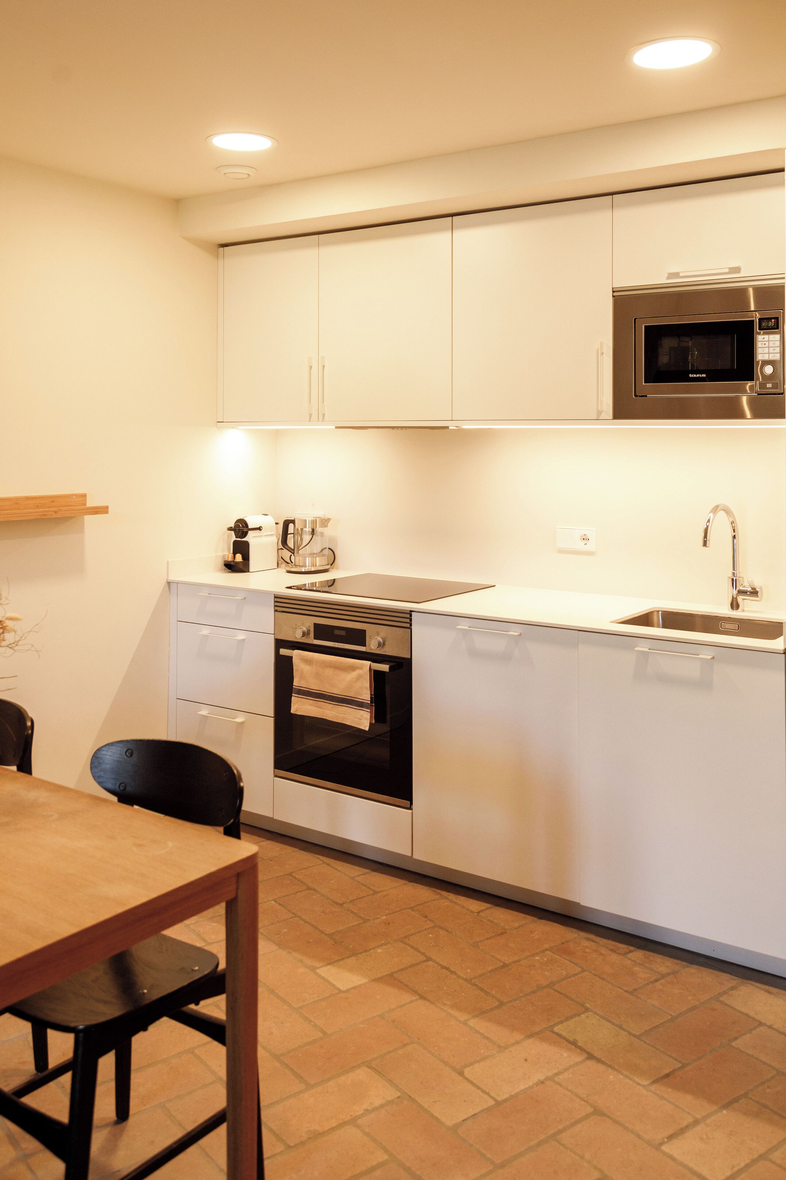 A compact kitchen with white cabinets, a built-in oven, a microwave, and a sink.