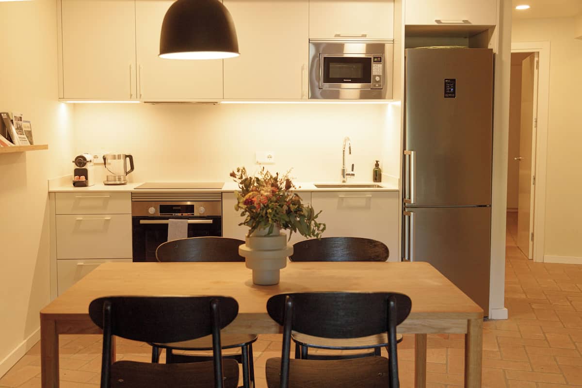 A modern kitchen with a dining table, chairs, a microwave, a refrigerator, and a coffee maker.