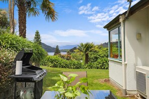 A backyard with a barbecue grill, a table, and a view of a lake and mountains.