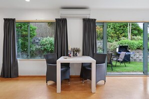 A room with a dining table and chairs, a large window with curtains, and an air conditioning unit. - Millar's Hideaway - Lake Views, Walk to Beach (Rotorua)