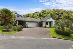 A two-story house with a garage, surrounded by lush greenery and a well-maintained lawn. - Millar's Hideaway - Lake Views, Walk to Beach (Rotorua)