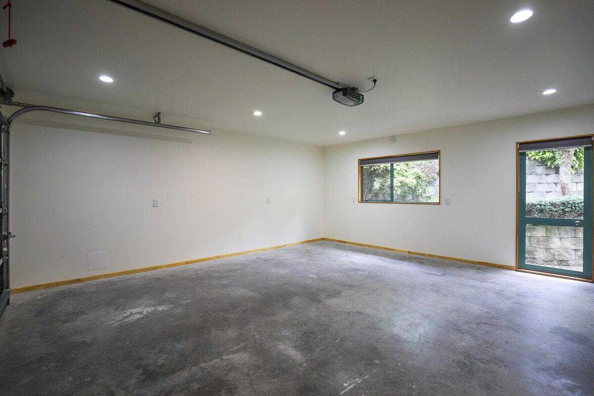 A spacious room with a concrete floor, a ceiling-mounted projector, and a window with a view of greenery.
