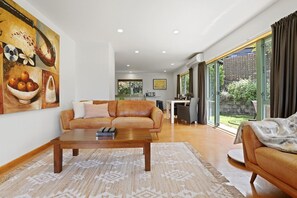 A living room with a leather sofa, a coffee table, and a painting on the wall. - Millar's Hideaway - Lake Views, Walk to Beach (Rotorua)