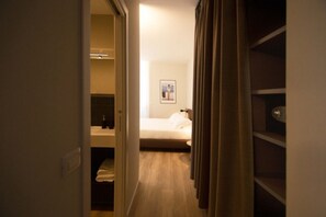 A hotel room with a bed, a bedside table, a nightstand, a framed picture on the wall, and a bathroom visible through an open door.