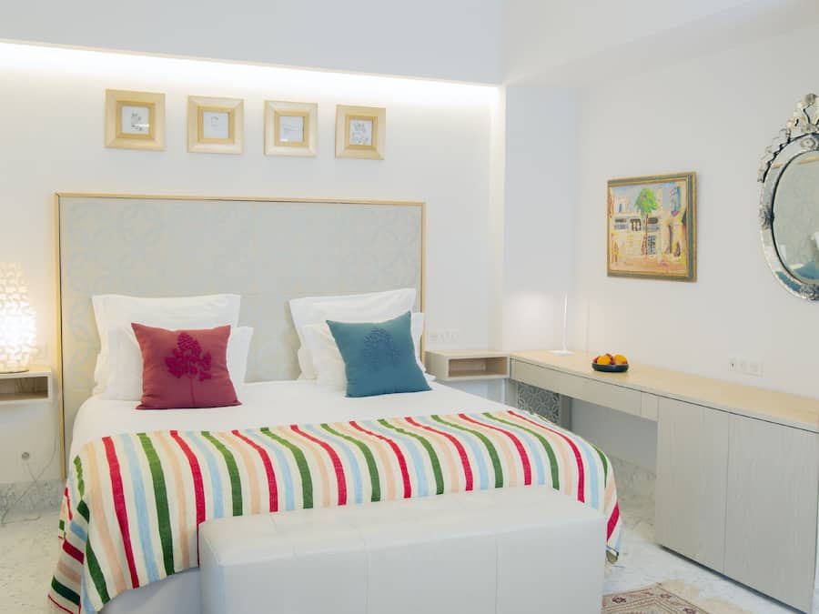 A modern bedroom with a large bed, a bedside table, a mirror, and framed pictures on the wall.