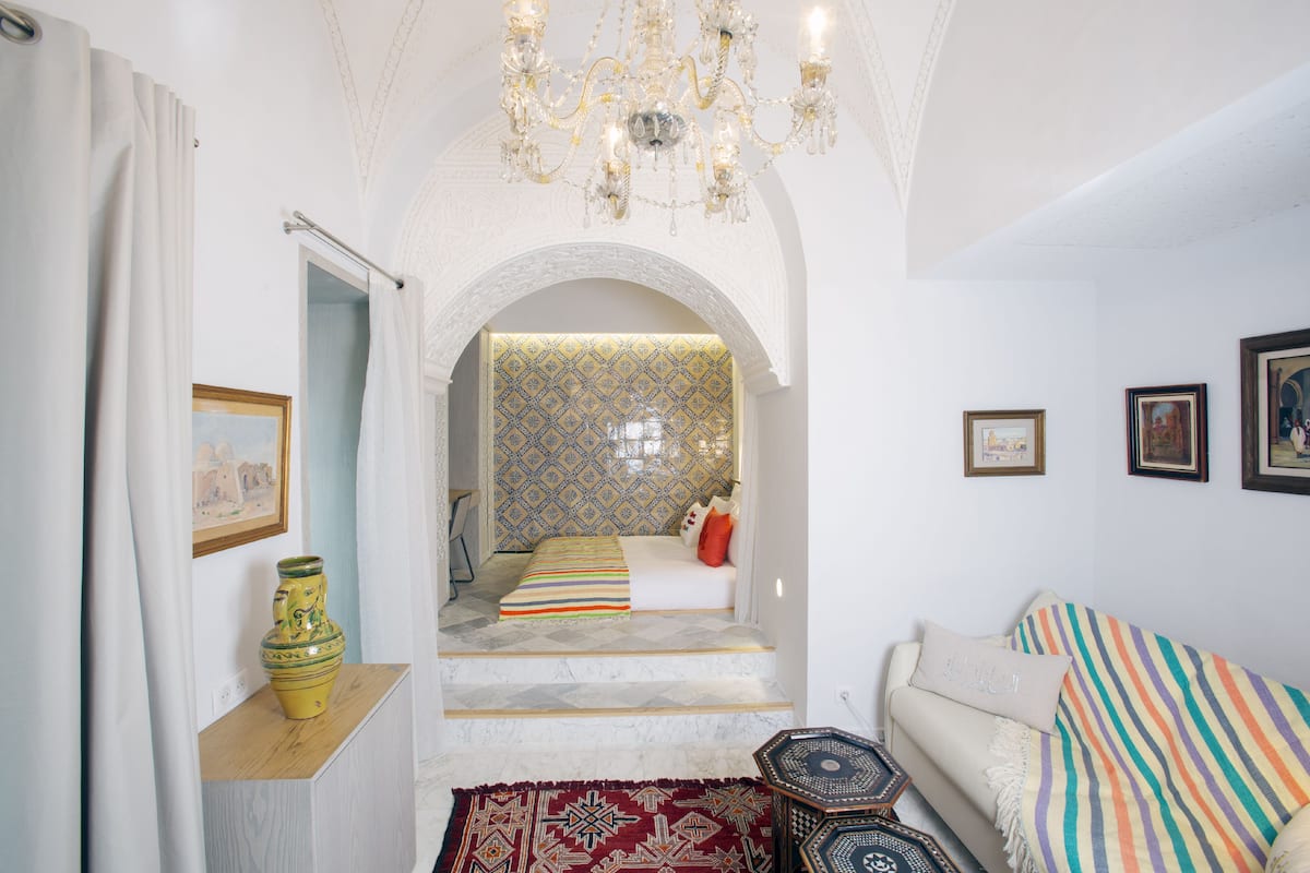 Um quarto com cama, sofá, lustre e papel de parede estampado.