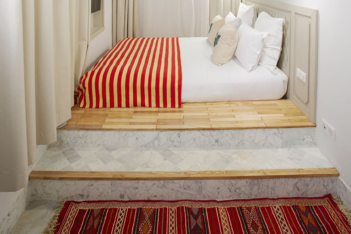 Quarto com cama, cortinas, janela e quadros nas paredes.