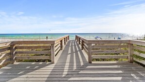 Una passerella di legno che conduce a una spiaggia con acque cristalline e alcune persone in lontananza.