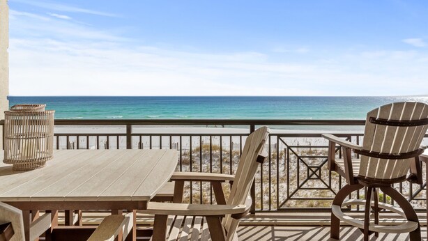 Un terrazzo in legno con tavolo e sedie che si affaccia su una spiaggia.
