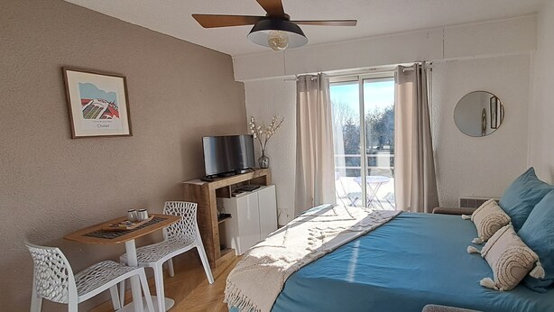 Un dormitorio con cama, escritorio con silla, televisor y ventana con cortinas.