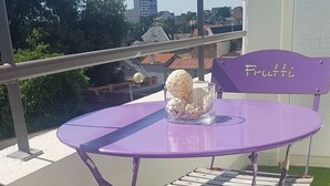 Un conjunto de mesa y sillas moradas en un balcón, con vistas a edificios y árboles.