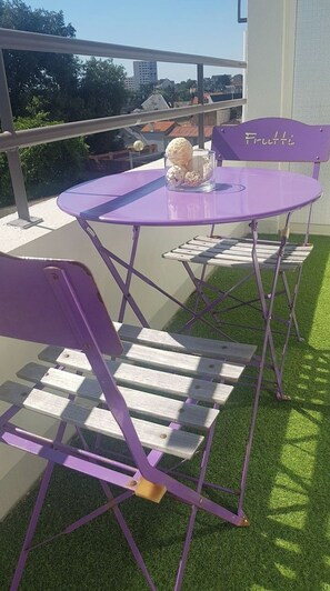 Un conjunto de mesa y sillas moradas en un balcón, con vistas a edificios y árboles.