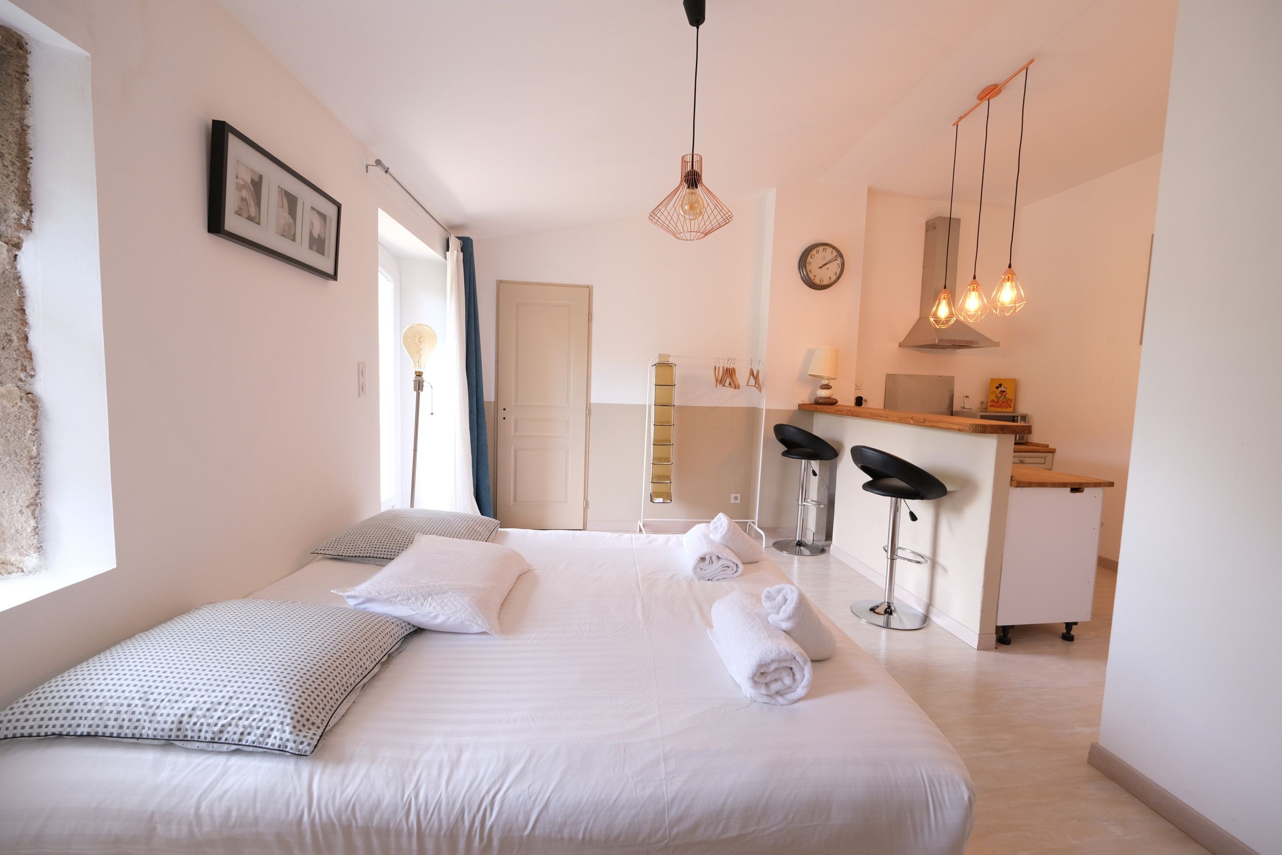 A hotel room with a bed, a desk, two bar stools, a kitchenette, and a large window.