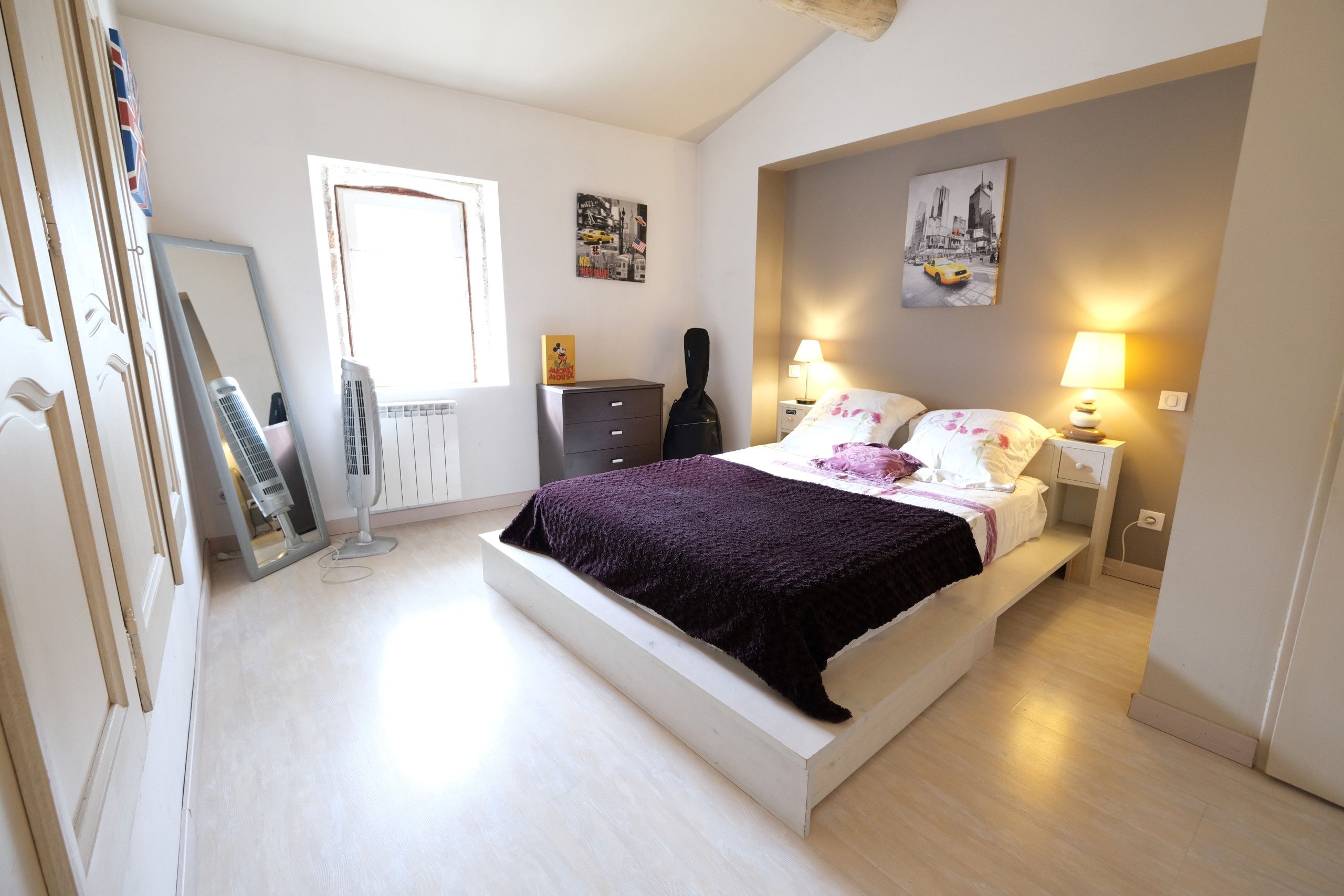 A bedroom with a bed, bedside lamps, a dresser, a guitar, and a window.