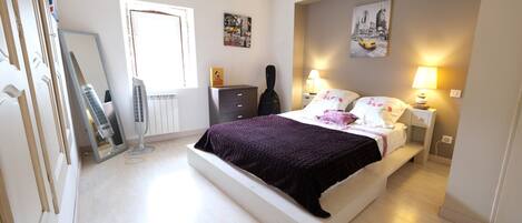 A bedroom with a bed, bedside lamps, a dresser, a guitar, and a window.