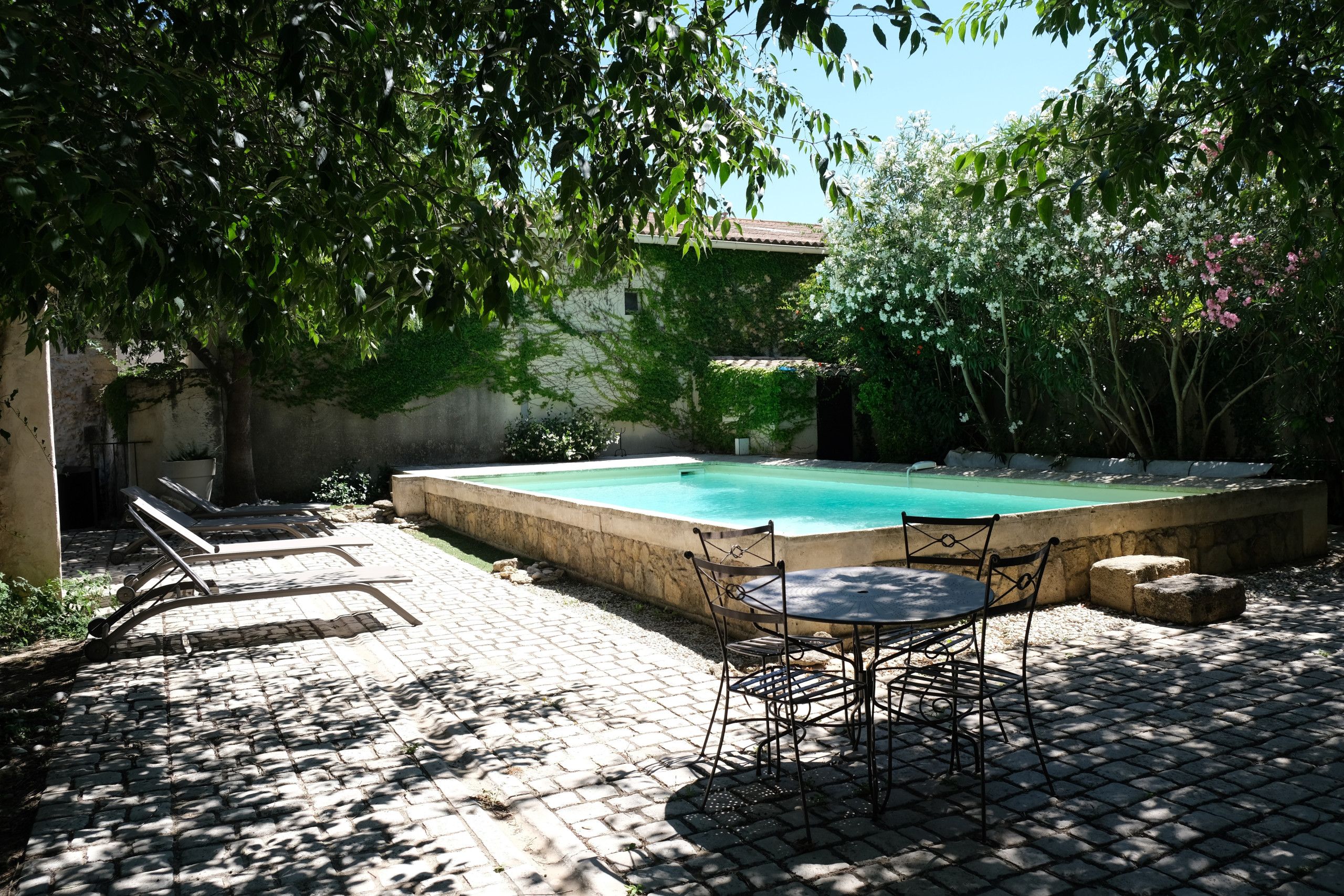 A swimming pool with a tiled deck, surrounded by a stone wall and lush greenery.