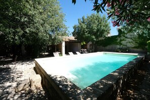 A rectangular swimming pool with a stone border, surrounded by a paved patio and shaded by trees. - Vacation rental with pool CHEVAL BLANC LS2-413 (Cheval Blanc)