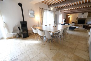 A spacious dining area with a wooden table and white chairs, a fireplace, and a modern kitchen in the background. - Vacation rental with pool CHEVAL BLANC LS2-413 (Cheval Blanc)
