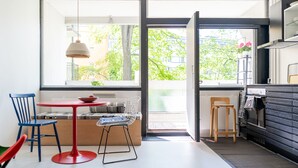 A modern kitchen with a large window, a dining area with a red table and blue chairs, and a kitchen counter with a sink and stove. - Helsinki home by Johanna Gullichsen (Helsinki)