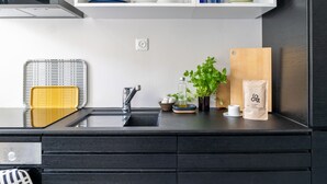 A modern kitchen with a black countertop, a stainless steel sink, a cutting board, a potted plant, a coffee bag, and a glass cabinet above the sink. - Helsinki home by Johanna Gullichsen (Helsinki)