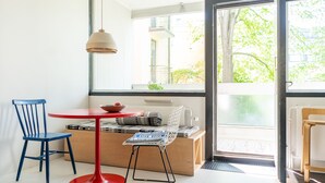 A room with a red table, a blue chair, a wooden bench, and a large window offering a view of the outdoors. - Helsinki home by Johanna Gullichsen (Helsinki)