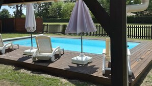 Un espacio al aire libre techado con piscina, sillas de descanso y sombrillas.