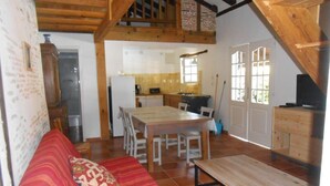Un salon chaleureux avec un canapé, un banc en bois et une table à manger avec des chaises. Il y a également un coin cuisine avec un réfrigérateur et une fenêtre.