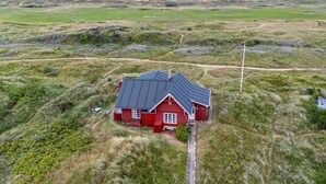 A red house with a black roof surrounded by grassy fields and a dirt path leading to it. - Beautiful home in Rømø with WiFi (Rømø)