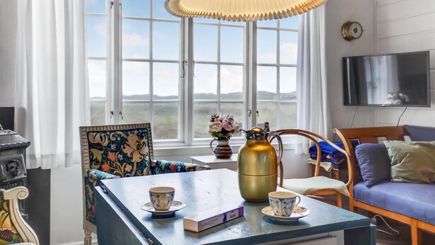 A cozy room with a large window, a blue table with two cups, a pitcher, and a vase with flowers. - Beautiful home in Rømø with WiFi (Rømø)
