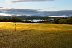 A golf course with a flagstick in the foreground, rolling hills, and a castle in the distance.