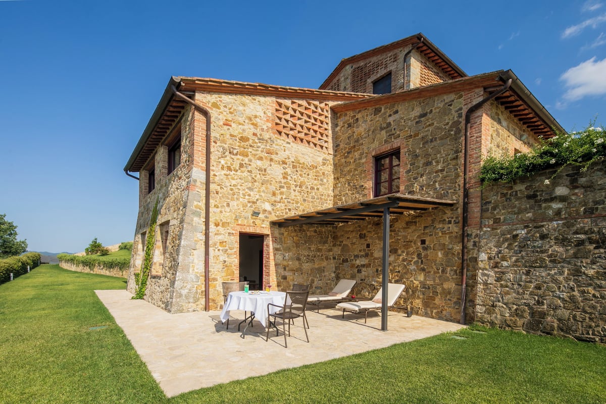 A stone building with a patio area, outdoor seating, and a view of the countryside.
