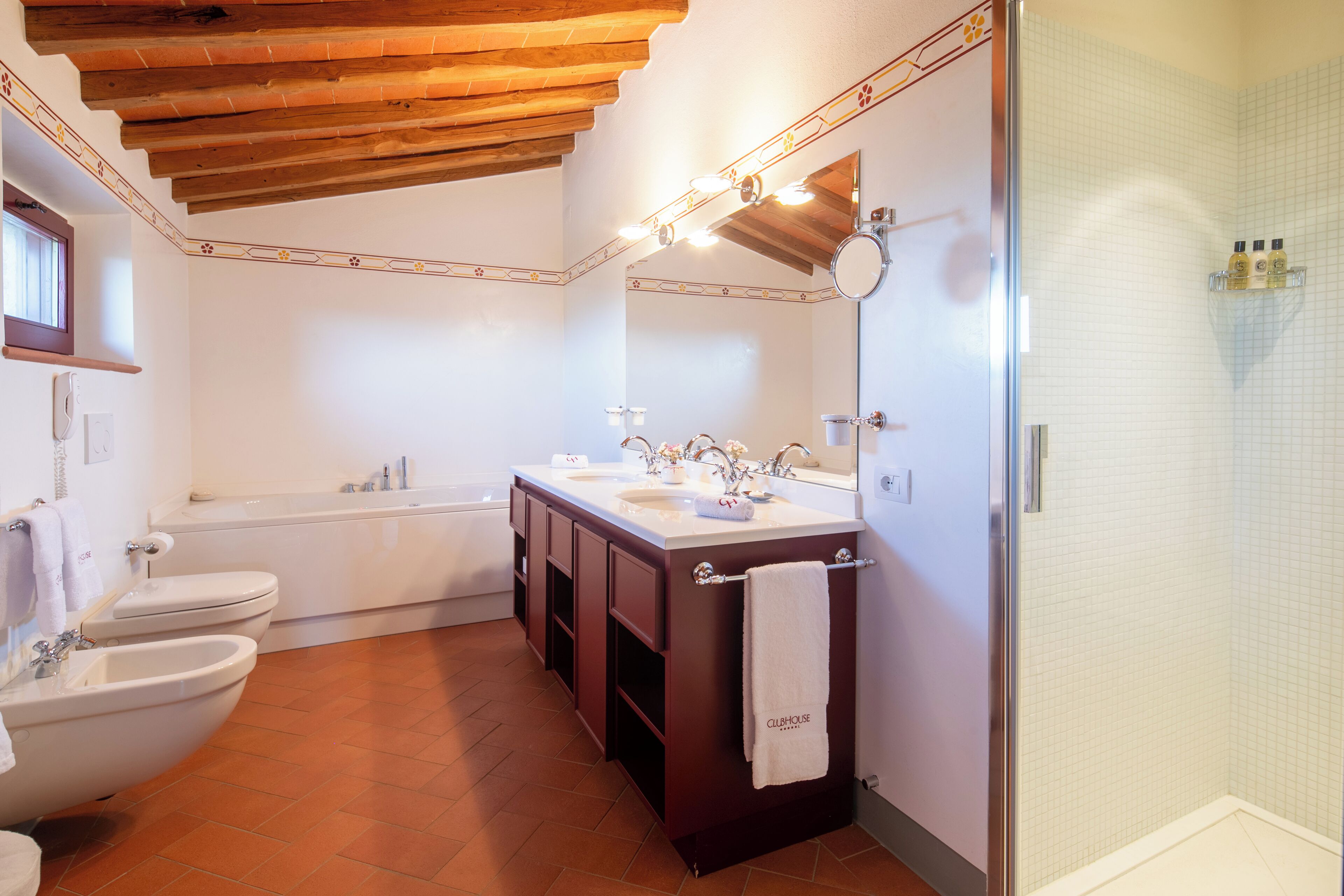 Un bagno con soffitto in legno, una vasca da bagno, un doppio lavabo e un box doccia in vetro.