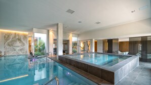 A large indoor swimming pool with clear water, surrounded by modern architecture and a glass railing. - The Club House (Castelnuovo Berardenga)