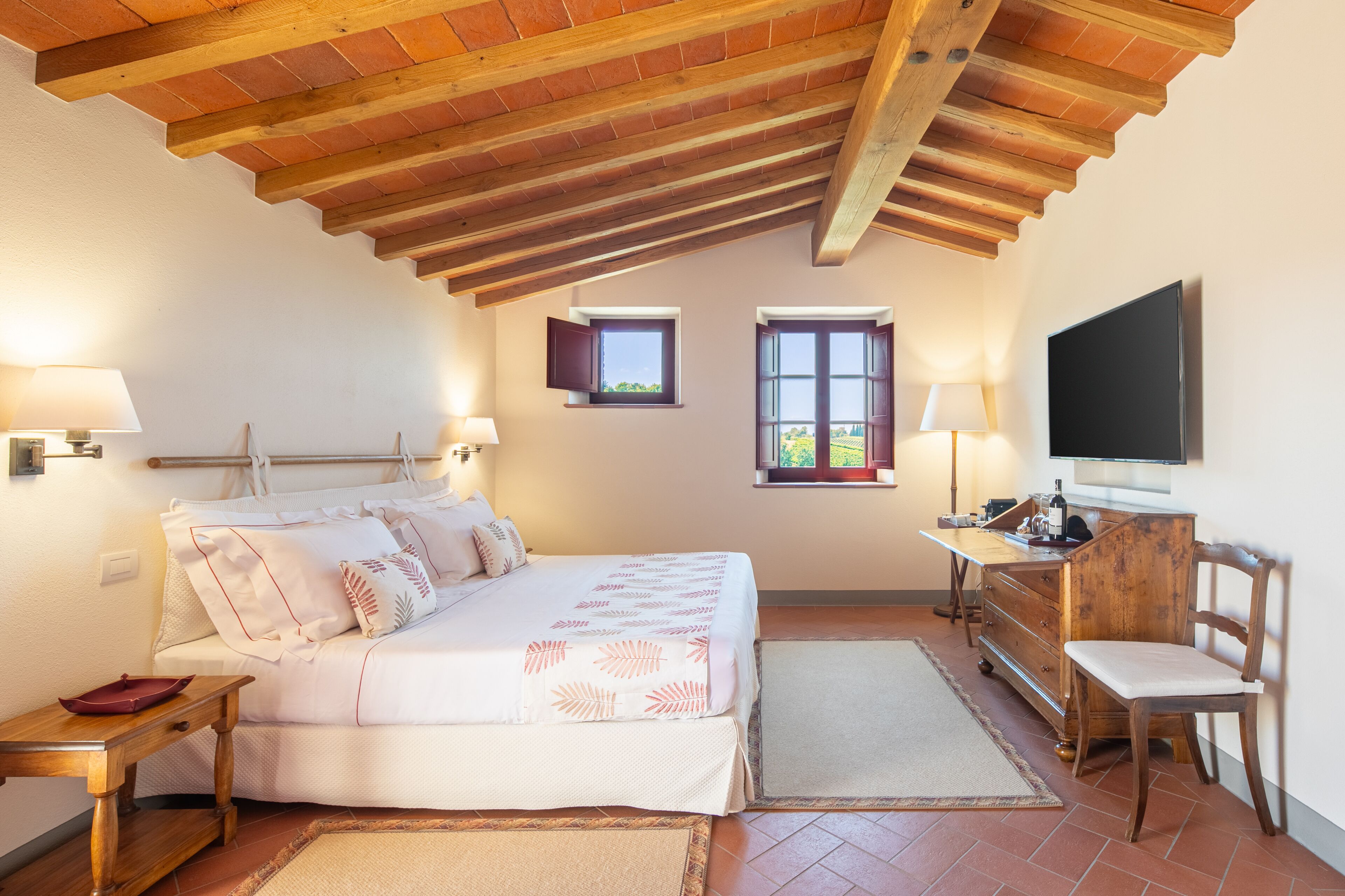 A bedroom with a bed, bedside tables, a dresser, a TV, and two windows.