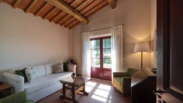 Un salon avec un plafond en bois, un canapé, une table basse en verre, un fauteuil vert, une lampe et une porte-fenêtre coulissante donnant sur un jardin.