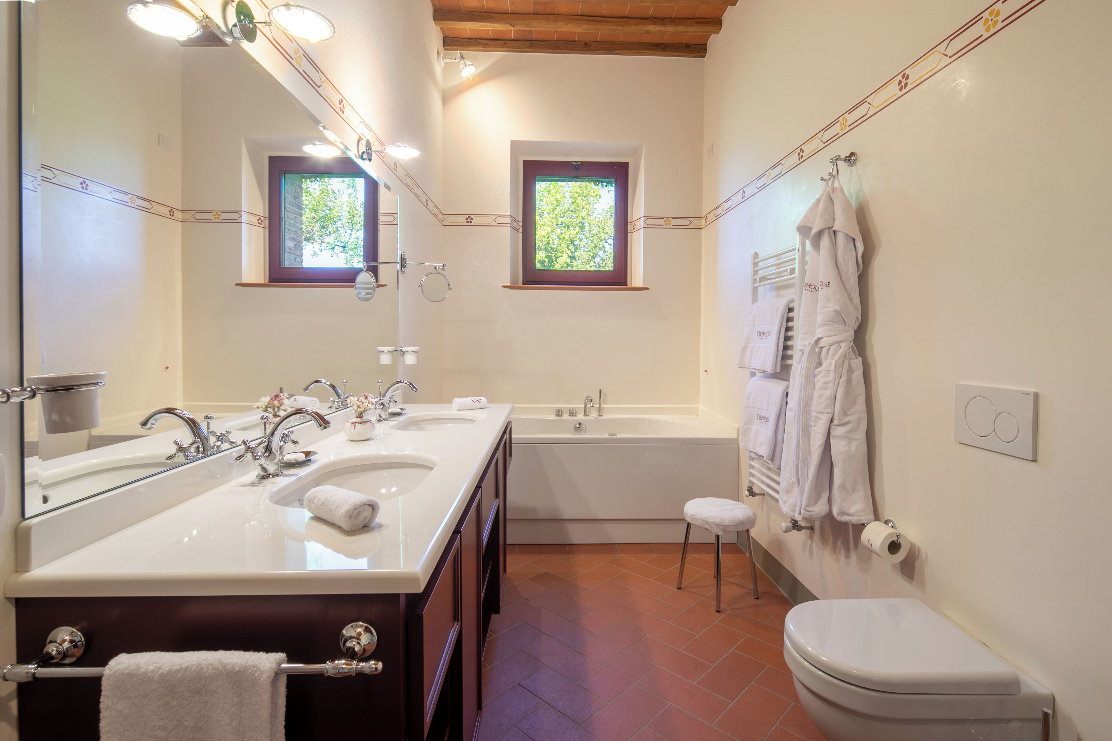 Un baño con lavamanos doble, bañera, inodoro y dos ventanas.