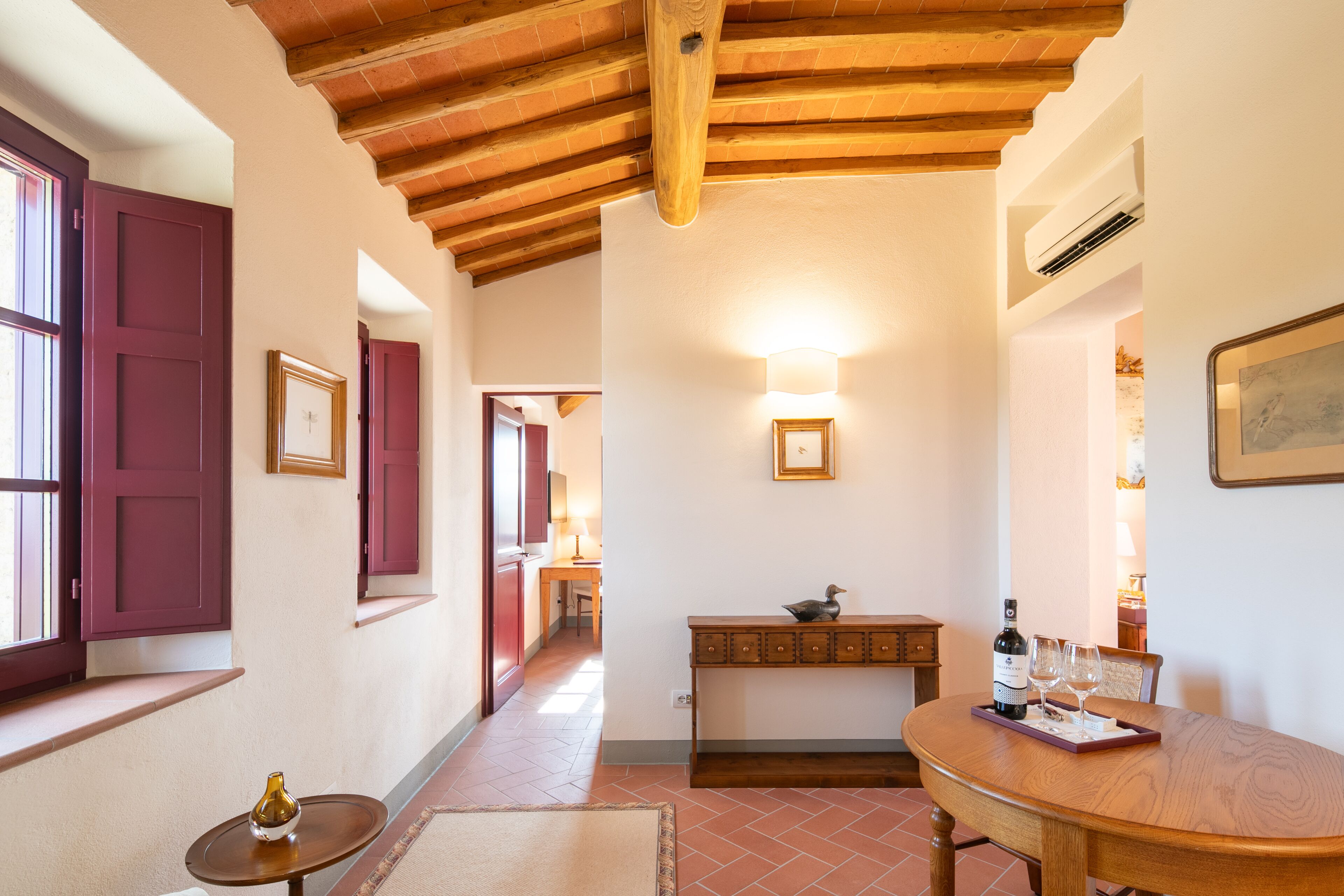 A hallway with a wooden ceiling, a dining area with a table set for two, and a wall-mounted light fixture.