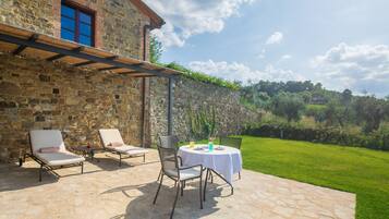 An outdoor patio with stone flooring, two lounge chairs, a table with a white tablecloth, and a stone wall.