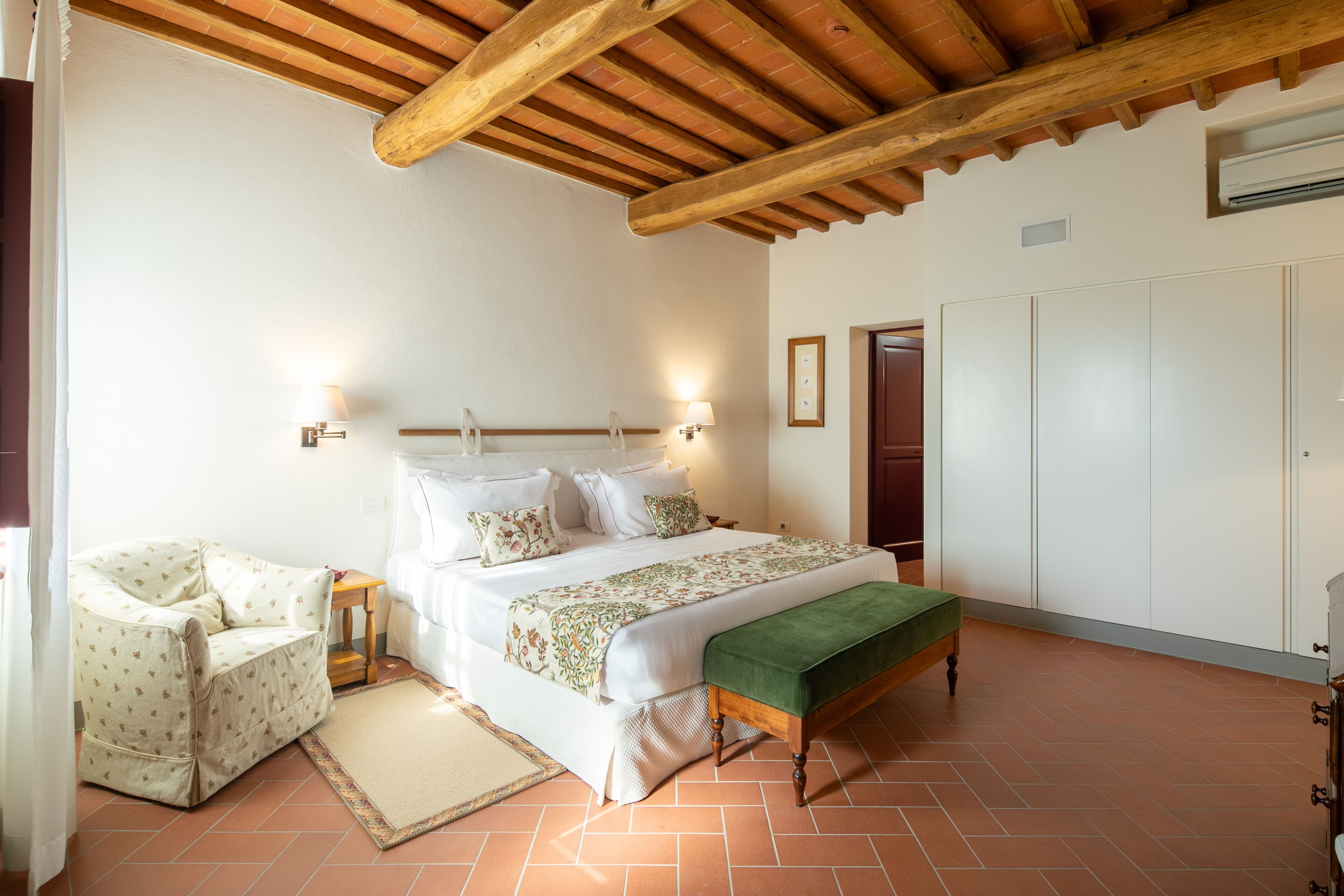 A bedroom with a bed, a chair, a bench, and a wardrobe.