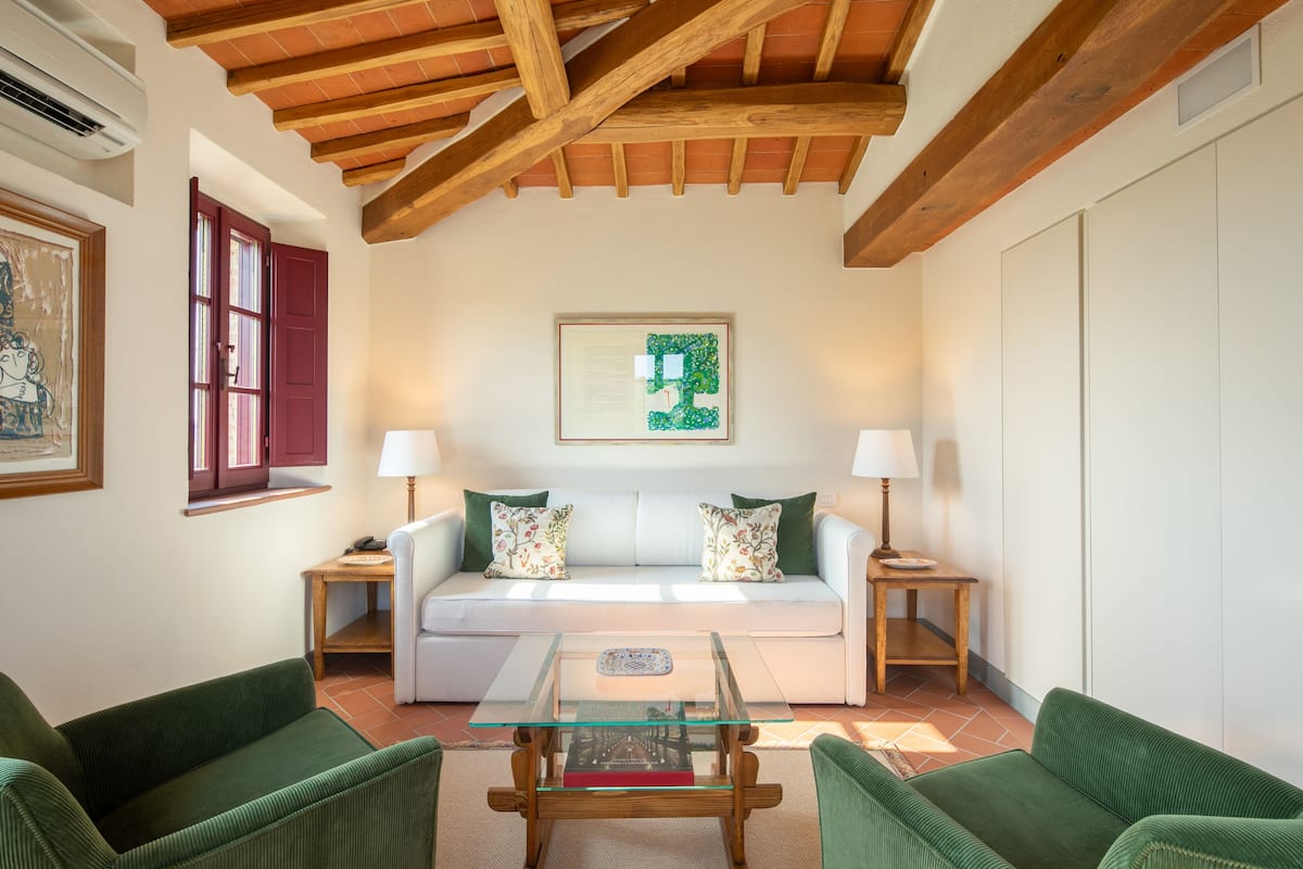 A living room with a white sofa, green cushions, a glass coffee table, and wooden beams on the ceiling.