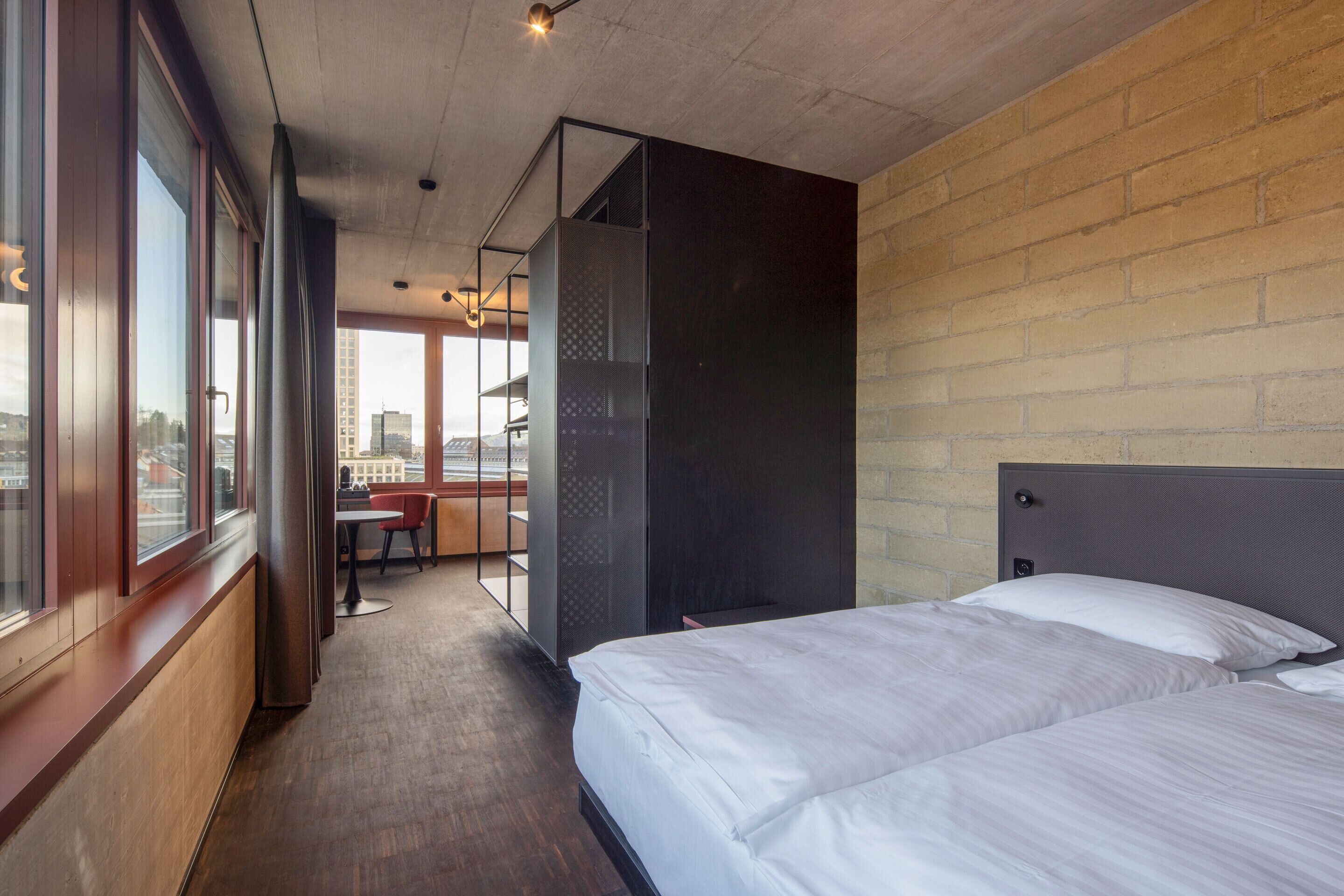 Una habitación de hotel moderna con una cama grande, un escritorio y vistas a la ciudad a través de amplios ventanales.