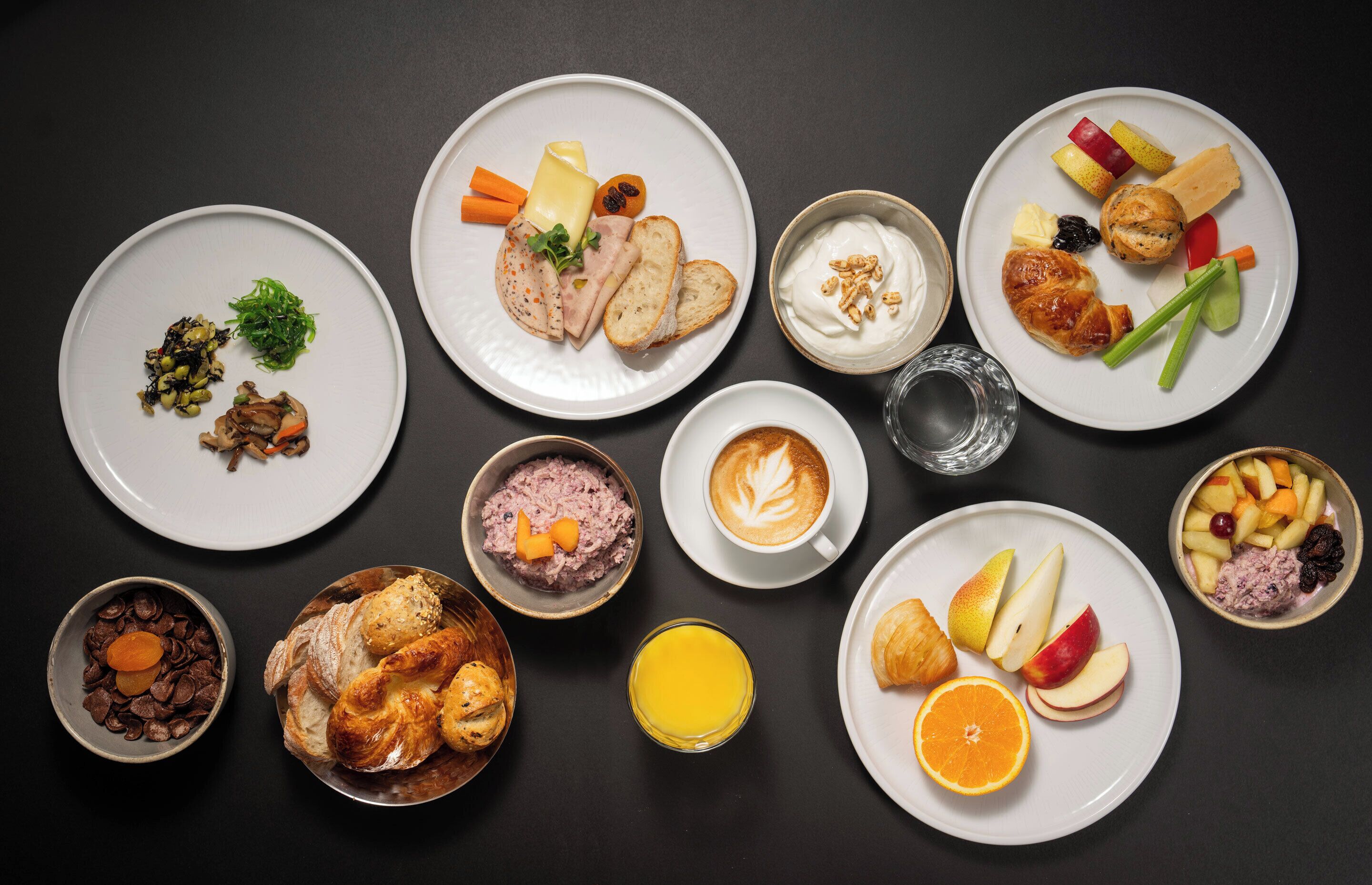 Une variété d’aliments pour le petit-déjeuner, notamment des viennoiseries, des fruits et des boissons, présentés sur des assiettes.
