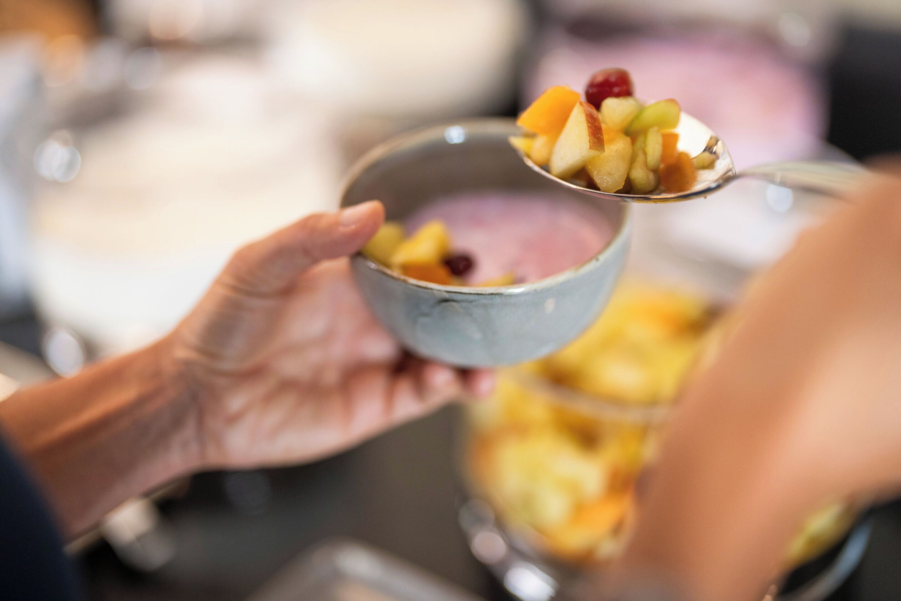 A person holding a bowl with a spoonful of mixed fruit.