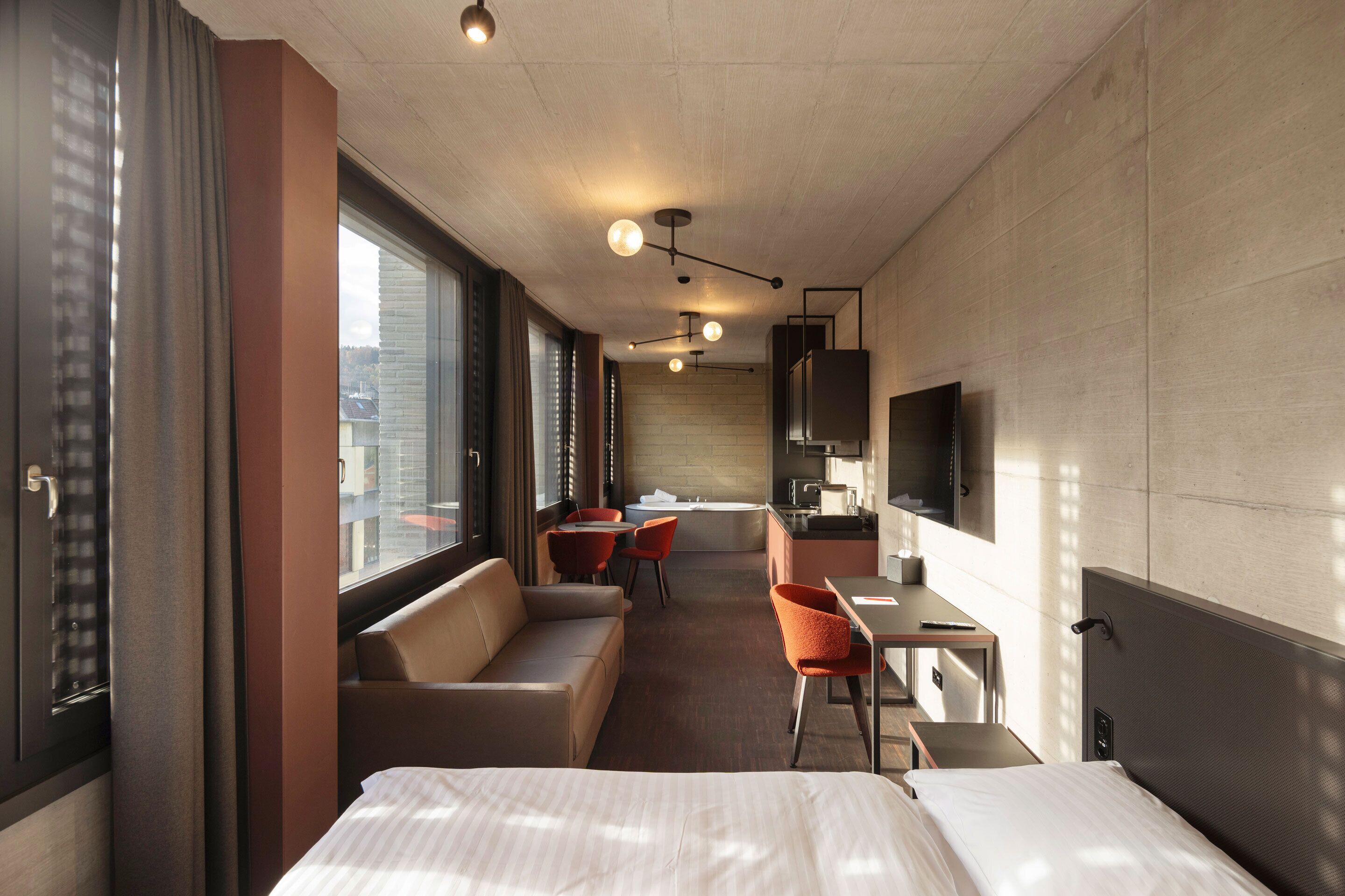 Habitación de hotel con cama, sofá, escritorio, silla, televisión y vista a la ciudad.
