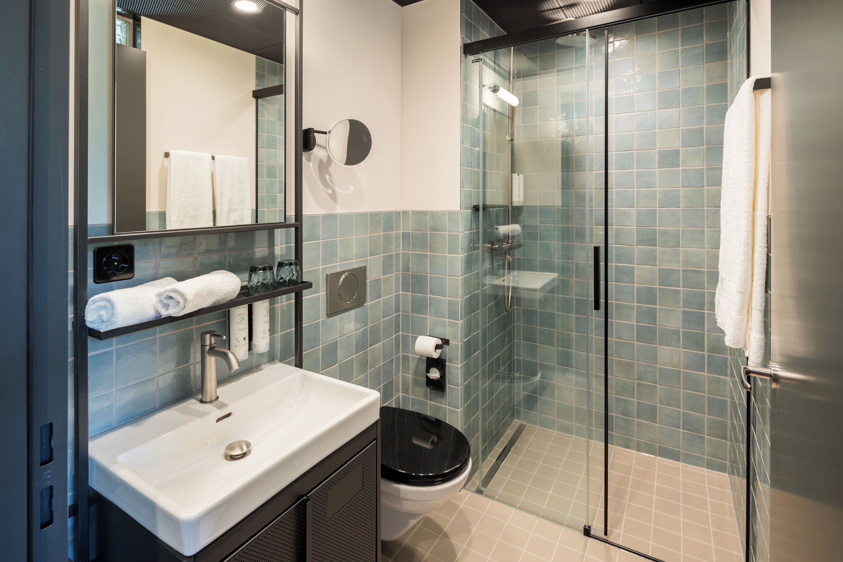A modern bathroom with a glass shower enclosure, a white sink, and a black toilet.